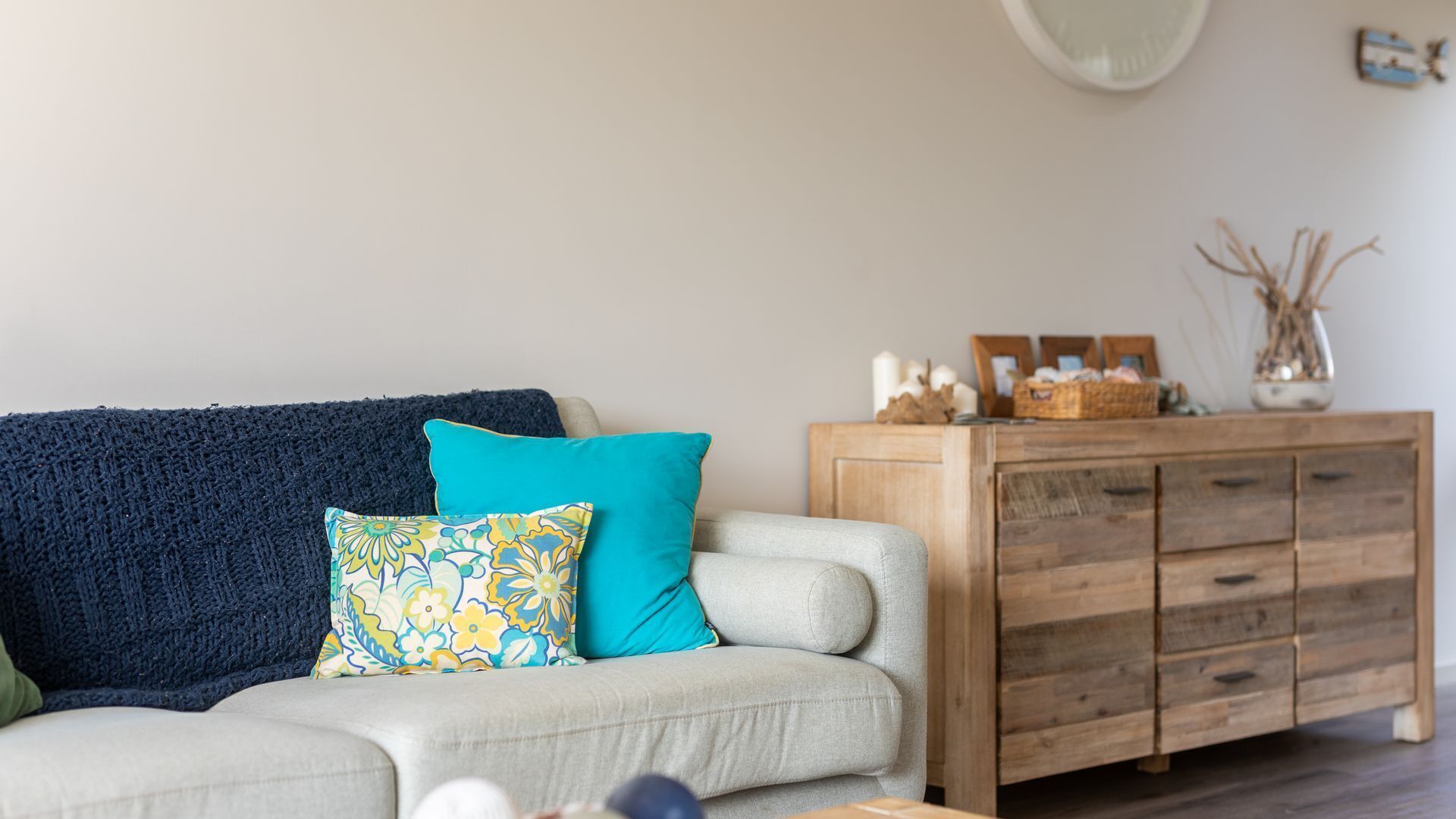 A living room with a sofa, two pillows, a wooden cabinet, and a vase with dried plants.