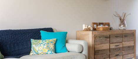 A living room with a sofa, two pillows, a wooden cabinet, and a vase with dried plants.