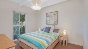 Una camera da letto con un'ampia finestra, un letto con lenzuola a righe, un elemento decorativo a parete e un piccolo tavolo con una lampada.