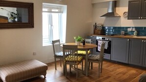 A compact kitchen with wooden flooring, a dining table with chairs, a bench, and a window with blinds. - Central Teignmouth - Sleeps 4 - Pets Allowed (Teignmouth)