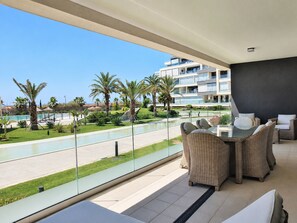 A balcony with wicker furniture overlooking a pool and a building with balconies.