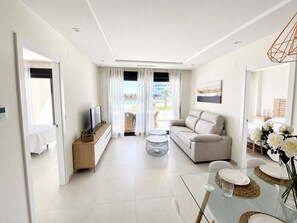 A modern living room with a sofa, a TV, and a dining area with a glass table.