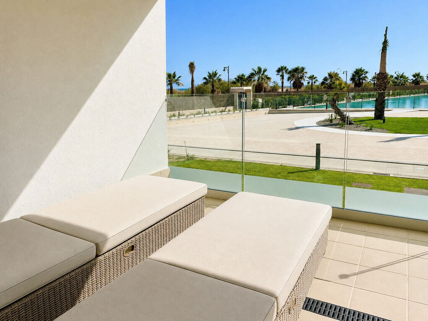 A balcony with cushioned seating and a view of a pool area with palm trees.