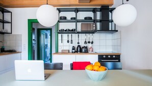 Uma cozinha moderna com um laptop sobre a mesa, uma tigela de laranjas e utensílios pendurados.