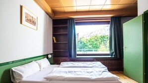 Um quarto com uma cama, janela com cortinas, estante e um quadro pendurado na parede.