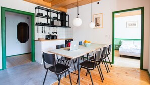 Cozinha moderna com área de refeições, apresentando uma mesa branca, cadeiras pretas e um laptop sobre a mesa.