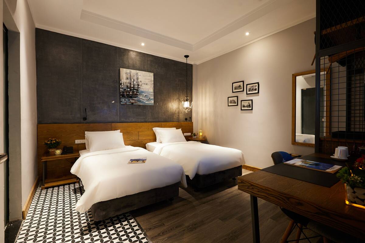 A hotel room with two beds, a wooden headboard, a dining table, and a large mirror.