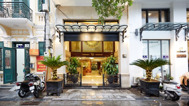 A hotel entrance with a grand facade, a covered entrance, and potted plants. - Hanoi Calido Hotel (Hanoi)