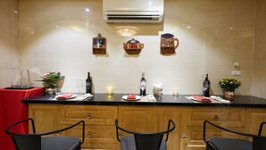 A kitchen with wooden cabinets, a black countertop, and a red tablecloth. There are three chairs, a potted plant, and a wine bottle on the counter. - Hanoi Calido Hotel (Hanoi)