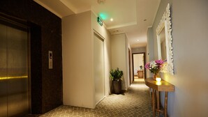 A hallway with an elevator, a potted plant, and a bar area with a mirror and flowers. - Hanoi Calido Hotel (Hanoi)