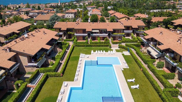 A resort with a central swimming pool, multiple villas with red-tiled roofs, and a mountainous backdrop.