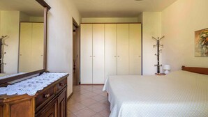 A bedroom with a large bed, a wooden dresser with a lace cover, a wardrobe, and a coat rack.