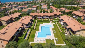 A resort with multiple buildings, a central swimming pool, and a view of the sea and mountains.