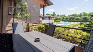 A balcony with a table and chairs, overlooking a swimming pool and garden.