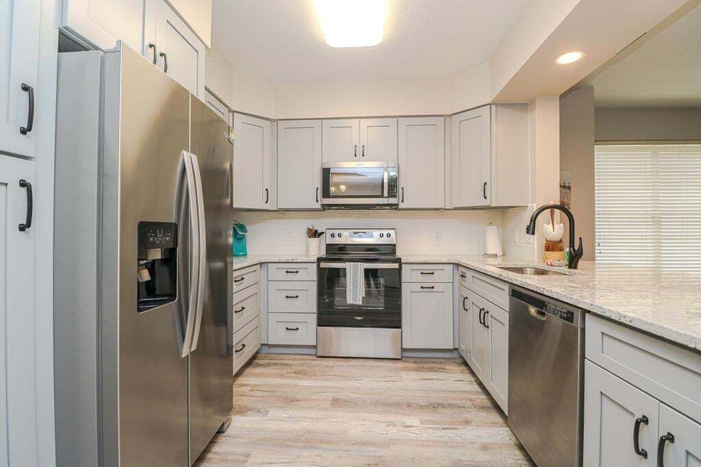 A modern kitchen with stainless steel appliances, white cabinetry, and a light wood floor.