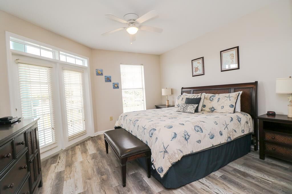 A bedroom with a bed, a bench, a dresser, a ceiling fan, and two windows with blinds.