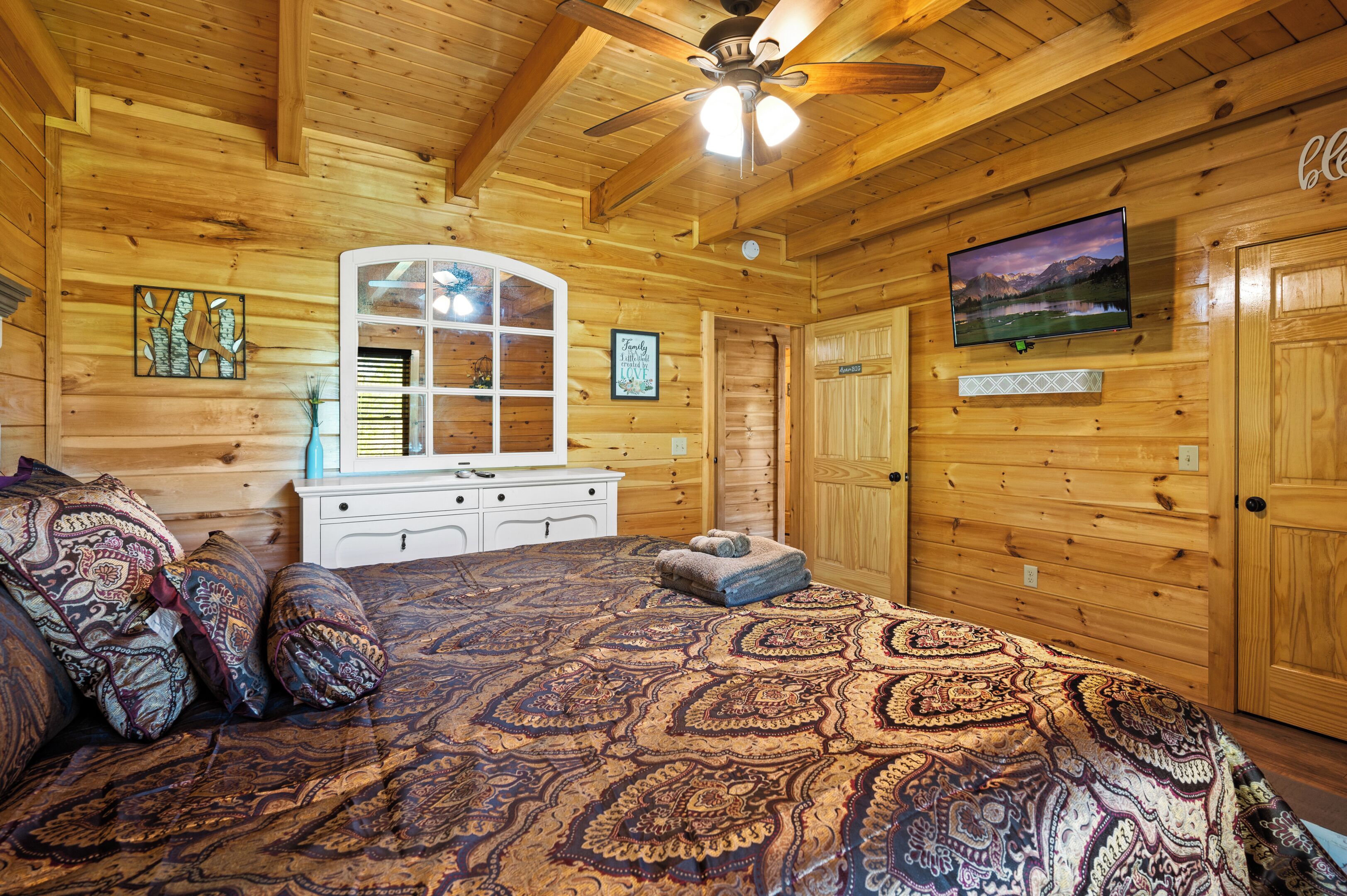 A wooden cabin bedroom with a bed, dresser, and a ceiling fan.
