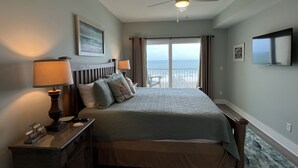 A bedroom with a bed, two bedside lamps, a ceiling fan, a TV, and a view of the ocean through a balcony door. - Wake Up to 1 Beautiful Vue - Beautiful Beachfront Condo! (Mexico Beach)