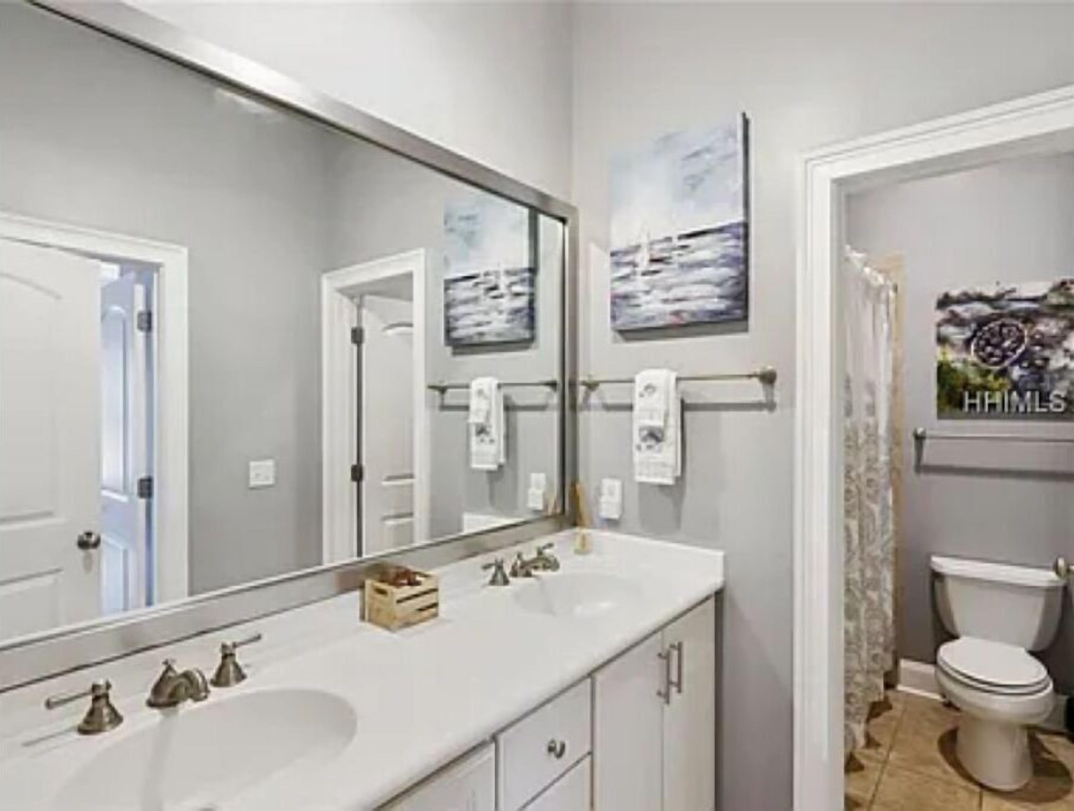 A bathroom with a large mirror, a white sink, a toilet, and a shower curtain.