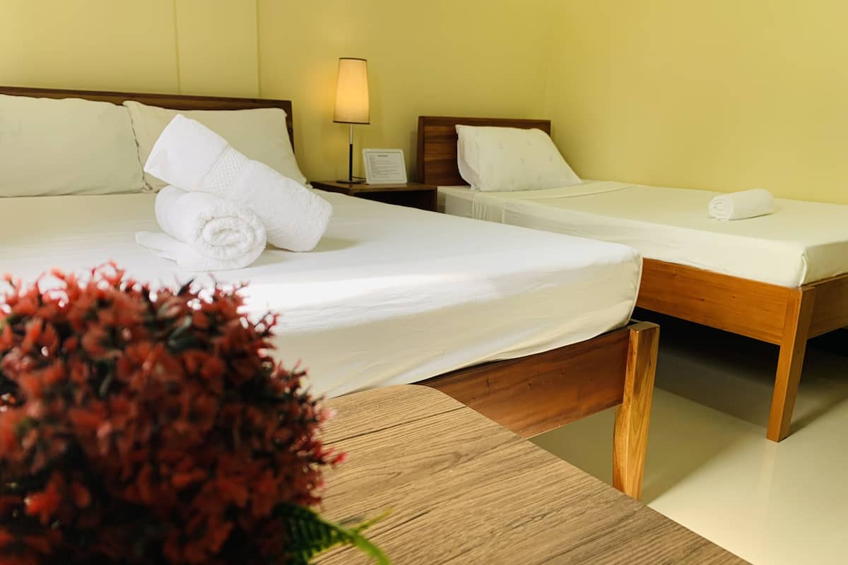 Hotellihuone, jossa on kaksi sänkyä, puinen pääty ja yöpöytä lampun kanssa sekä koristeellinen kukka-asetelma.