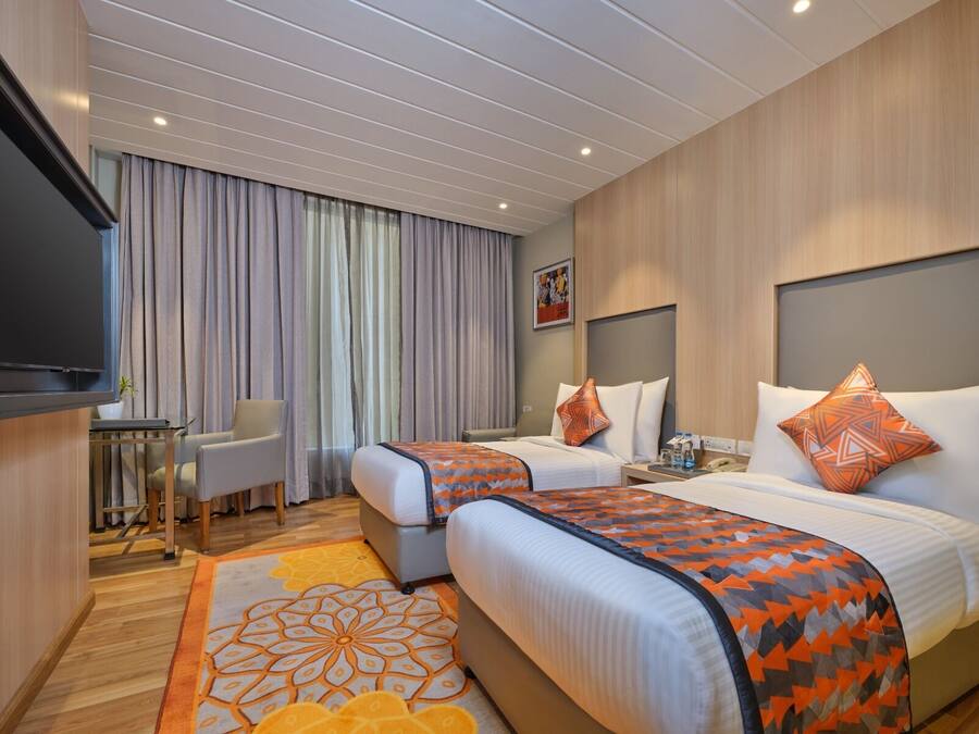 A hotel room with two beds, a TV, a desk, and a chair.