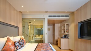 Quarto de hotel com cama, chuveiro, banheiro, cozinha compacta e televisão.