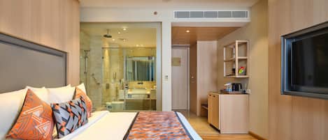 A hotel room with a bed, a shower area, a bathroom, a kitchenette, and a TV.