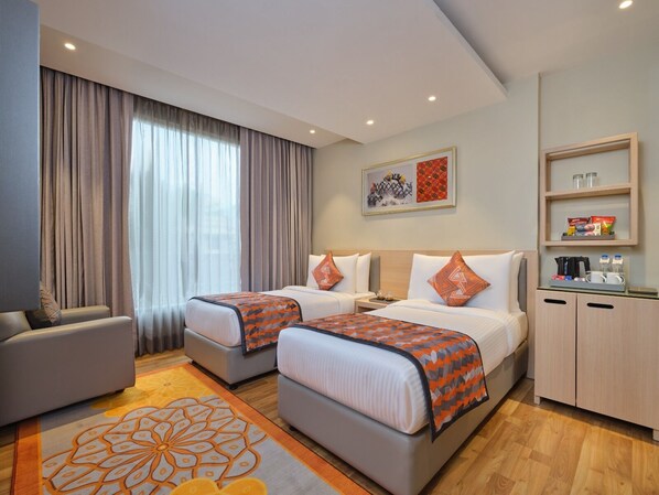 A hotel room with two beds, a sofa, a coffee table, a minibar, and a large window with curtains.
