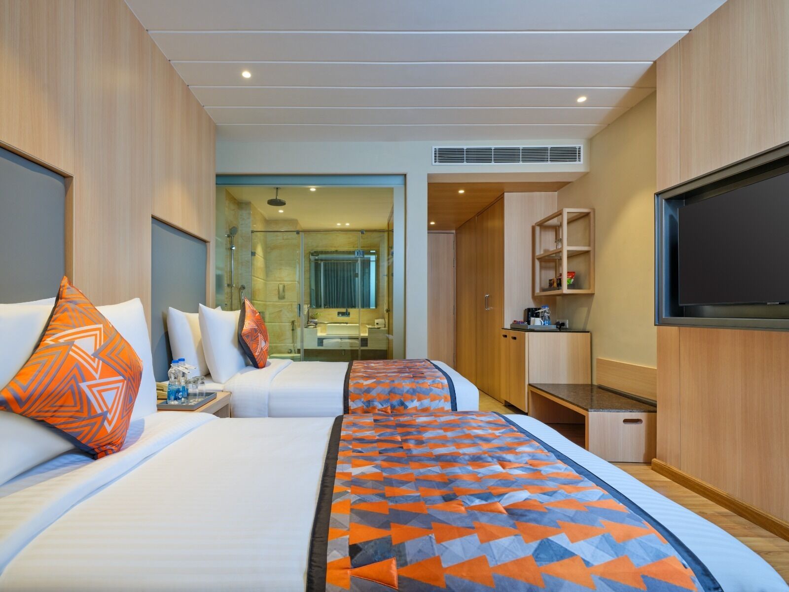 A hotel room with two beds, a TV, a bathroom, and a kitchenette.