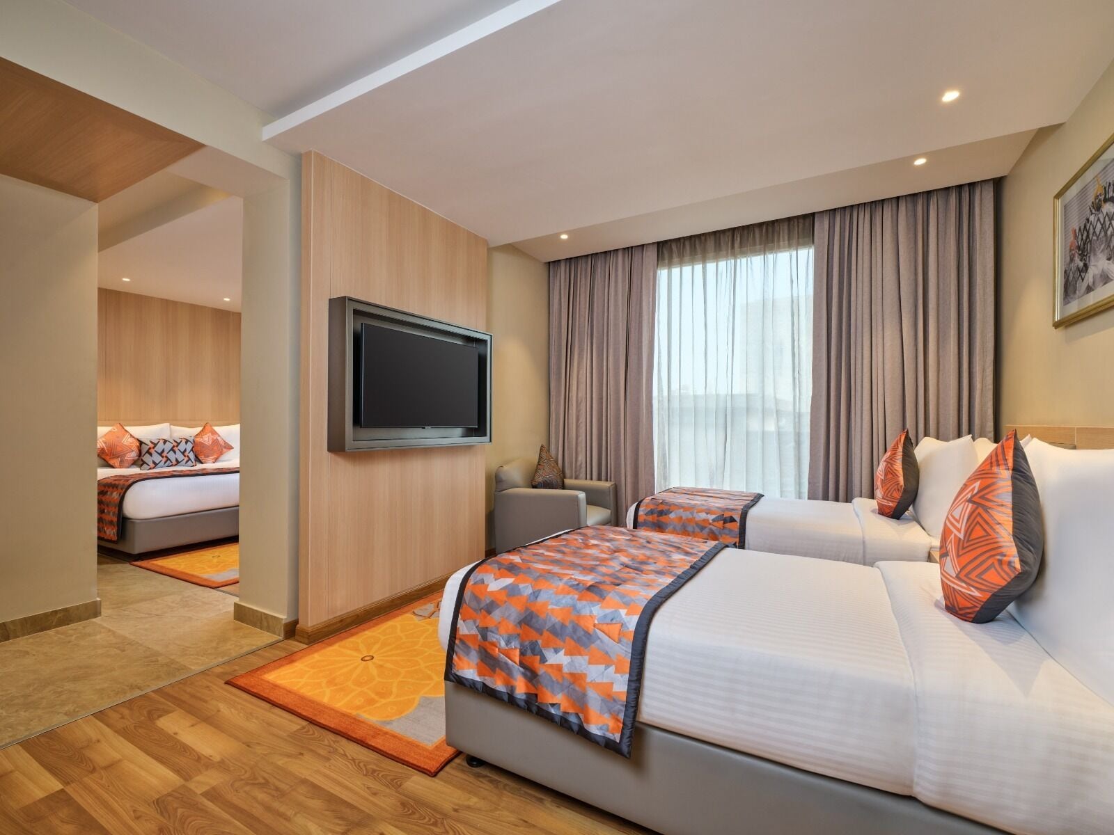 A hotel room with two beds, a flat-screen TV mounted on the wall, a sofa, and a large window with curtains.
