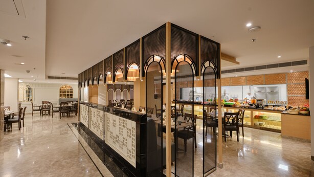 Um hall de hotel espaçoso com uma área de recepção central, espaços para sentar e uma área de cozinha visível.