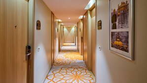Corredor de hotel com portas de madeira, placas de quarto numeradas e carpete estampado.
