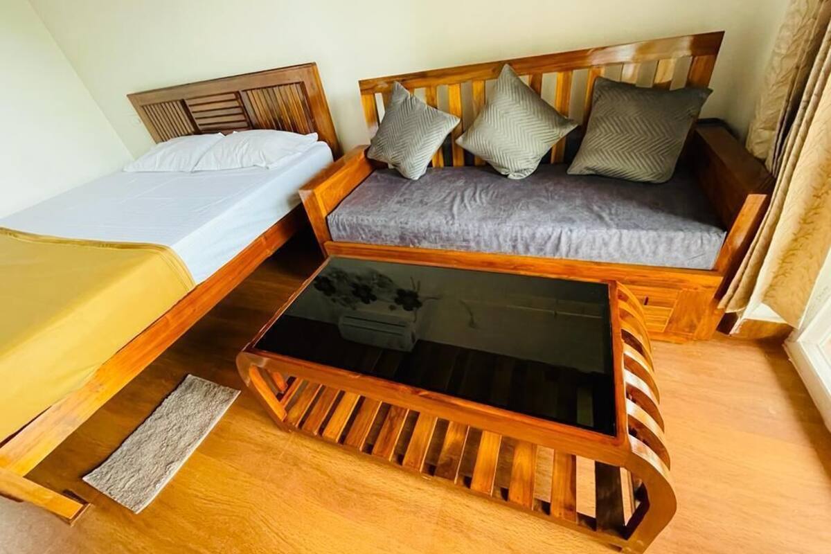 A room with a wooden bed, a wooden sofa with cushions, and a glass-top coffee table.