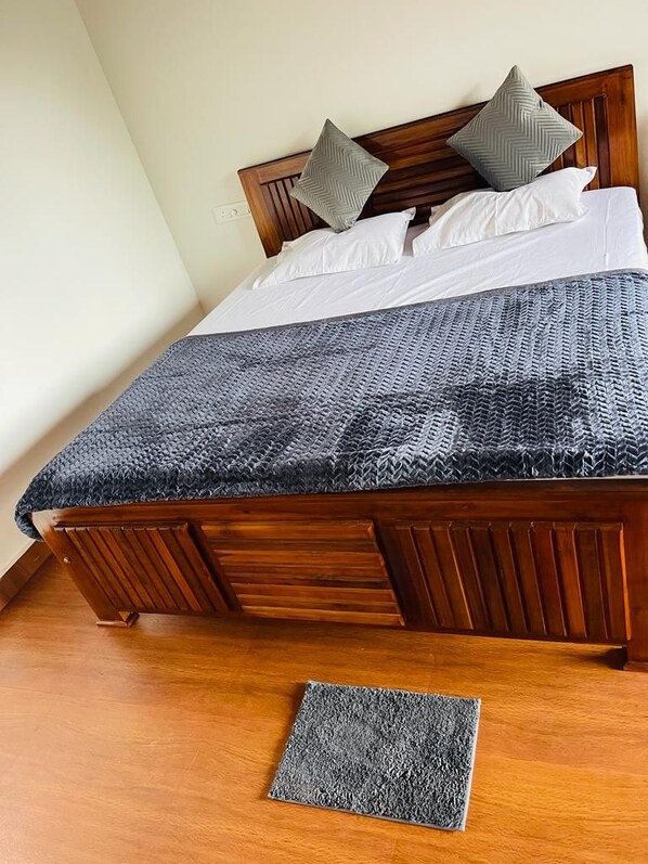 A wooden bed with a grey textured bedspread and pillows, a matching grey rug on the floor, and a wooden headboard.