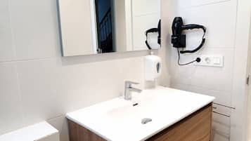 Une salle de bain avec un lavabo blanc, un miroir, un distributeur de savon et un sèche-cheveux fixé au mur.