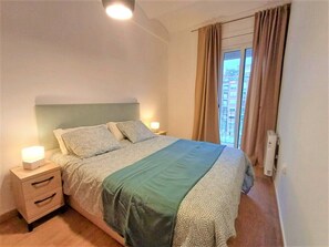 A bedroom with a bed, bedside tables, a nightstand, a window with curtains, and a wall-mounted air conditioning unit. - LV31 Apartamento en Poblenou-Playa de Barcelona (Barcelona)