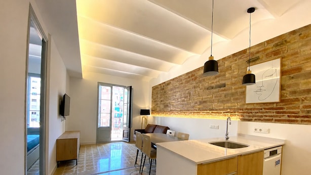 Una cocina moderna con una isla central, armarios de madera, una pared de acento de ladrillo, iluminación colgante y vistas de la ciudad a través de un amplio ventanal.