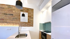 Una cocina con pared de ladrillo, un lavamanos de acero inoxidable, una lámpara colgante negra, un microondas y un refrigerador blanco.