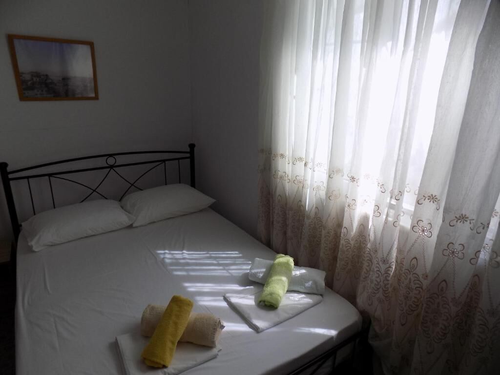 A bed with white bedding, a metal headboard, and a window with sheer curtains.