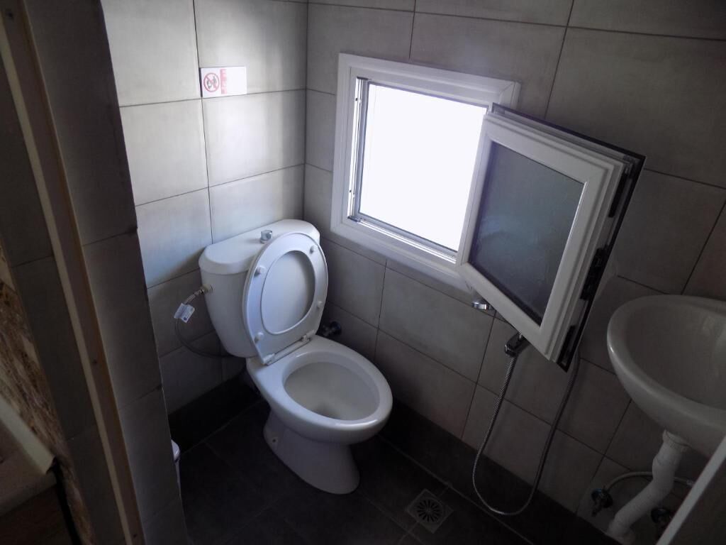 Een kleine badkamer met toilet, een raam en een wastafel.