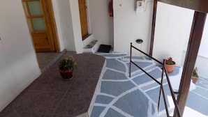 A staircase with a blue and white patterned floor, a potted plant on the landing, and a wooden door in the background. - VS studios Economy Double Room (Skiathos)