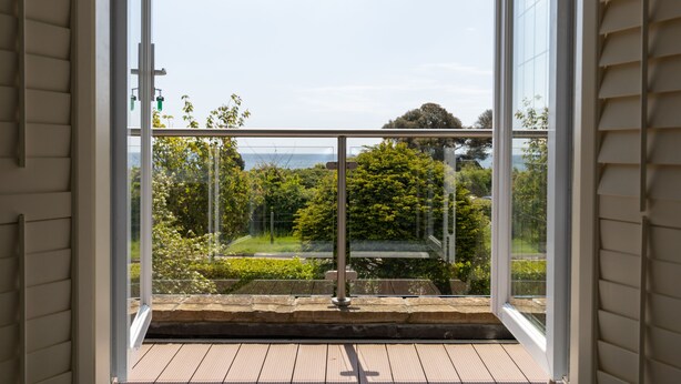 A balcony with a glass door, a metal railing, and a view of greenery and trees. - The Beach House - a stone's throw from Avon Beach, Friars Cliff (Christchurch)