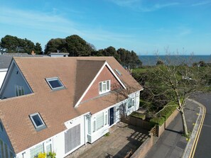 A two-story house with a sloped roof, a small front porch, and a view of the sea.