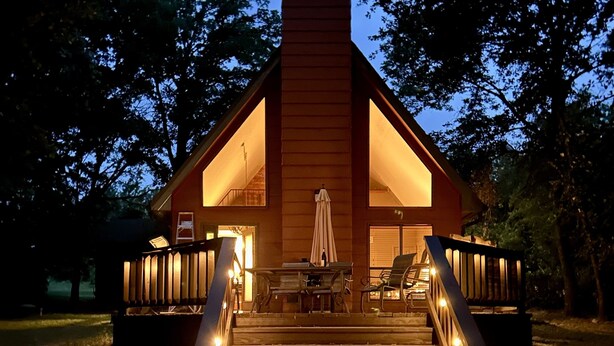 A wooden cabin with a staircase leading to a deck, surrounded by trees. - This relaxing cabin is cozy and secluded with private pond and fishing dock (Kingston)