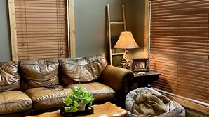 A living room with a brown leather sofa, a wooden coffee table, a small plant, a lamp, and a dog bed. - This relaxing cabin is cozy and secluded with private pond and fishing dock (Kingston)