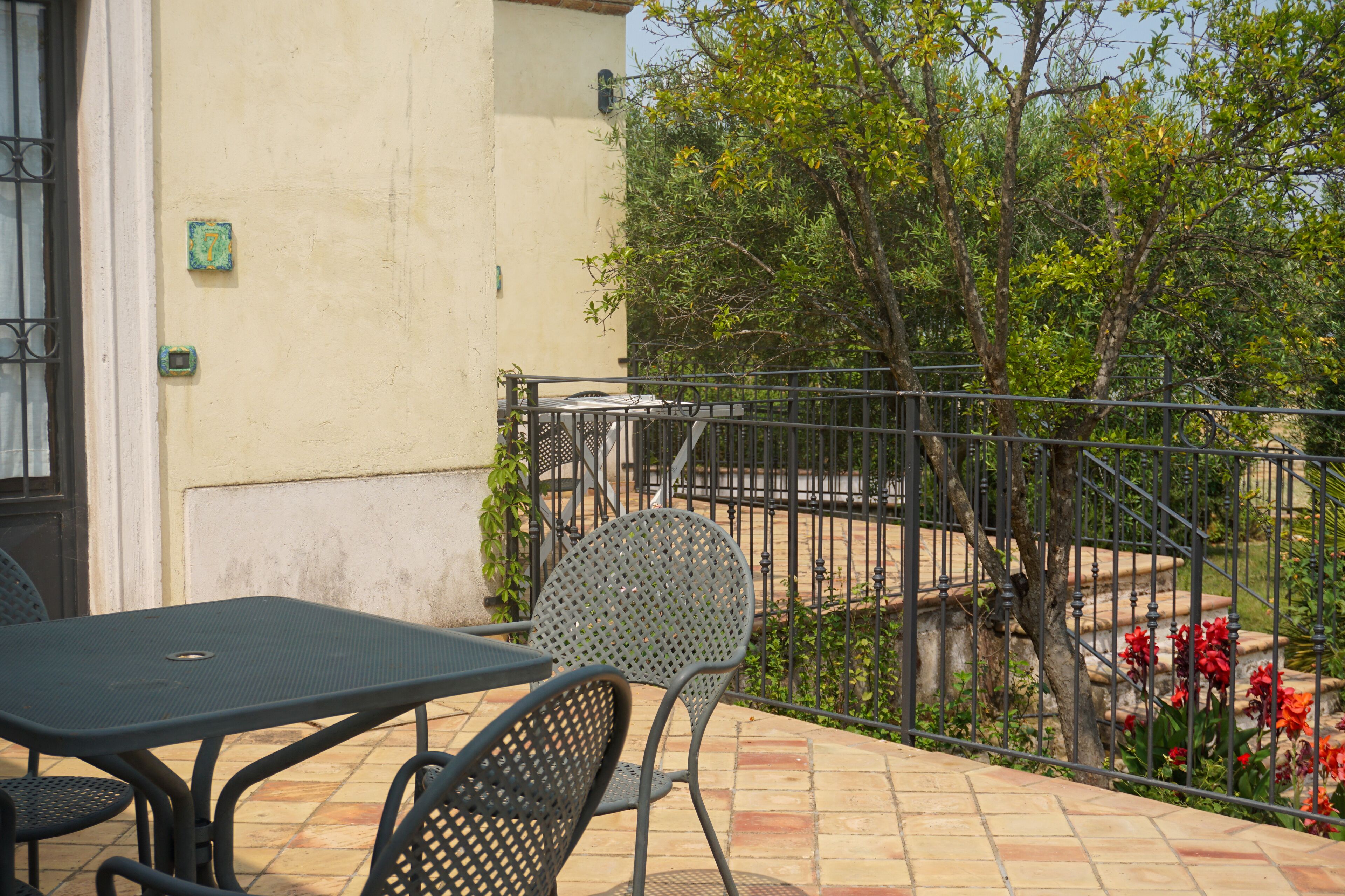 A patio with a table and chairs, a metal railing, and a staircase leading to a garden with red flowers.