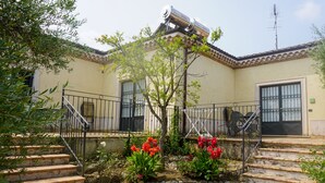 Un edificio con techo de tejas, una cámara de seguridad y un pequeño jardín con flores rojas.