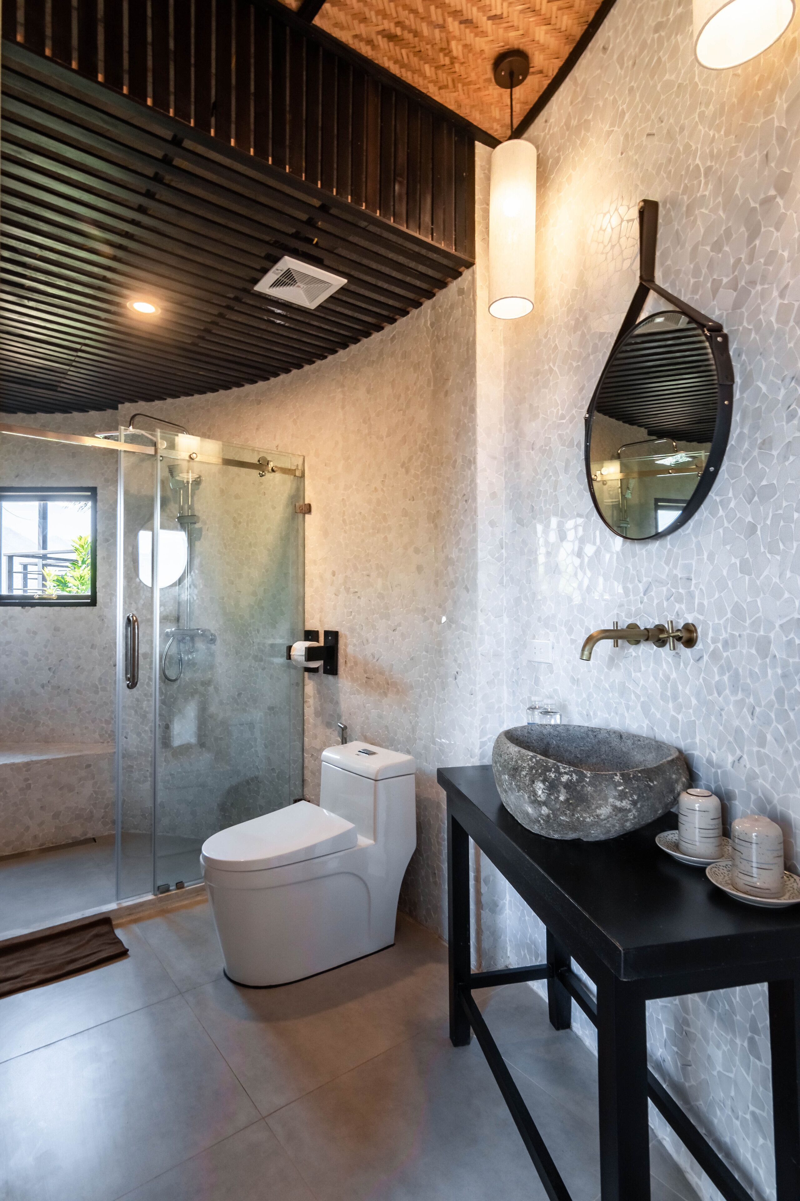 Une salle de bain moderne avec une douche à parois de verre, des toilettes blanches, un lavabo en pierre et un meuble-lavabo noir.