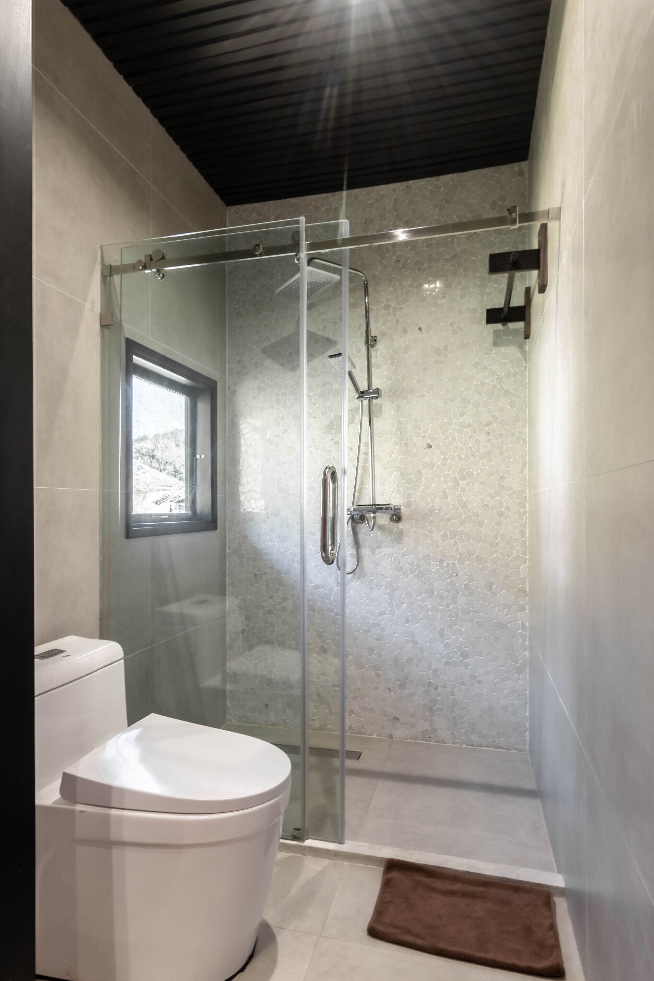 A modern bathroom with a glass-enclosed shower, a toilet, and a window.