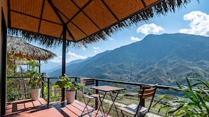 Una terraza con techo de paja, plantas en macetas y vistas a montañas.